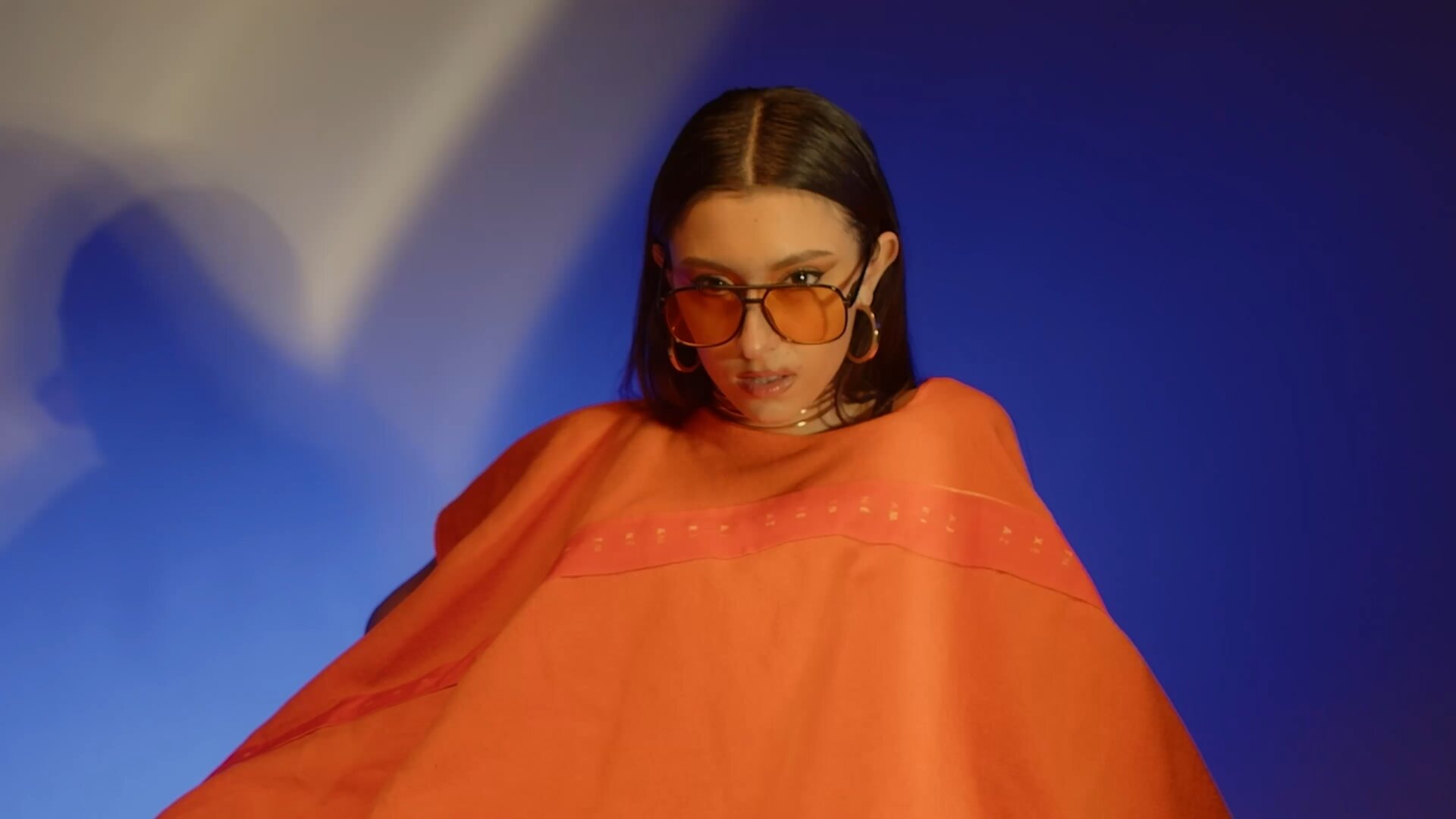 Model wrapped in orange cape against deep blue studio backdrop